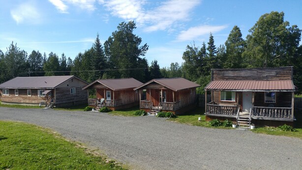 A row of wooden cabins with porches and a gravel driveway. - All Seasons Campground & Cabins (Ninilchik)