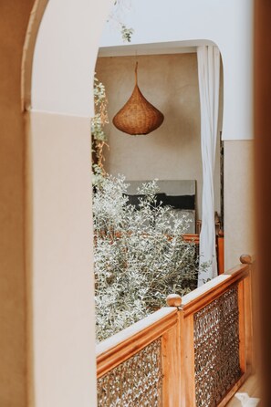 A room with a bed, a hanging light fixture, and a view of a balcony with plants. - Dar Nour El Houda (Marrakech)