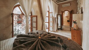 A bedroom with a large bed, a wooden dresser, and a view through a window with curtains. - Dar Nour El Houda (Marrakech)