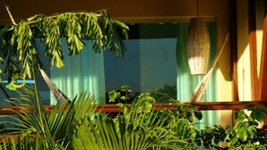 Una habitación con una hamaca, plantas verdes y una ventana con cortinas.