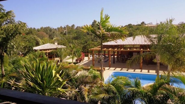 Un área de piscina con una pérgola y mobiliario exterior, rodeada de exuberante vegetación tropical.