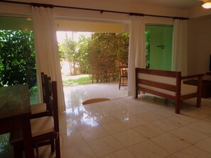 Una habitación con piso de baldosas, muebles de madera y vista a un jardín desde una puerta.