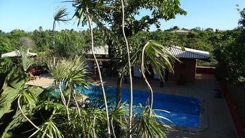 A swimming pool surrounded by lush greenery and a small building with a tiled roof.