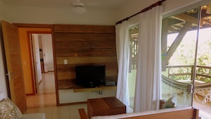 Una habitación con pared de madera, televisor, banco y vista a un balcón.