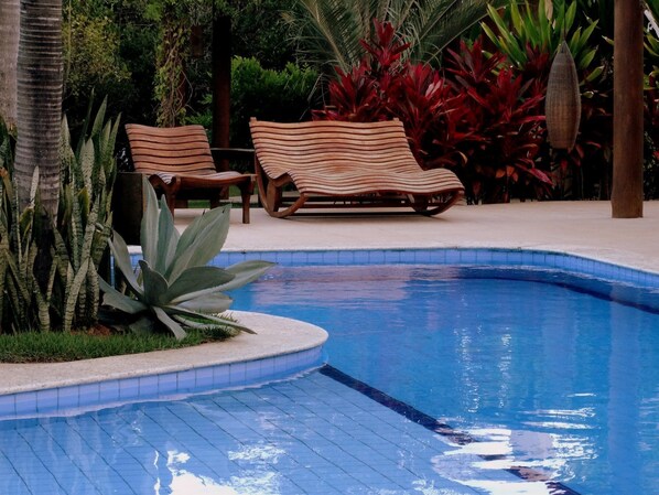 Un área de piscina con dos sillones de descanso y plantas tropicales.
