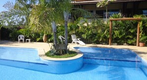 Una piscina de borde curvo, rodeada de palmeras y sillones de descanso.