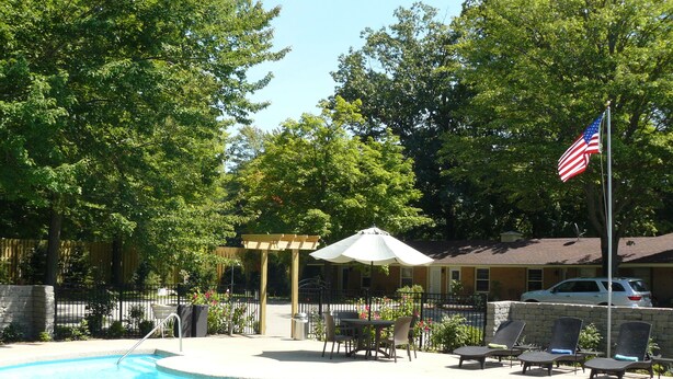 A swimming pool with lounge chairs and an umbrella, surrounded by trees and a fence. - The Saugatuck Retro Resort Motel (Saugatuck)