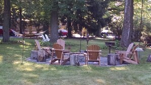An outdoor seating area with wooden Adirondack chairs and a fire pit, surrounded by trees and a wooden fence. - The Saugatuck Retro Resort Motel (Saugatuck)