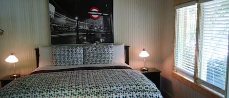 Un dormitorio con cama, dos lámparas de noche, un cartel del metro de Londres y una ventana con persianas.
