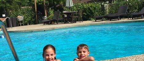En swimmingpool med ett trädäck, solstolar och en pergola.