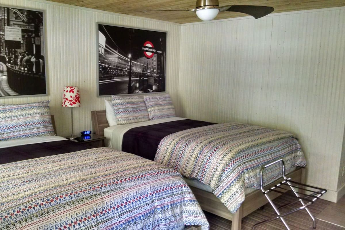 A room with two beds, a nightstand, a lamp, and a wall clock.