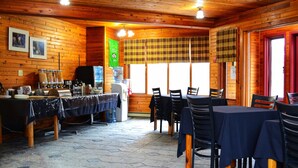 A wooden interior with tables and chairs, a water dispenser, and a window with plaid curtains.