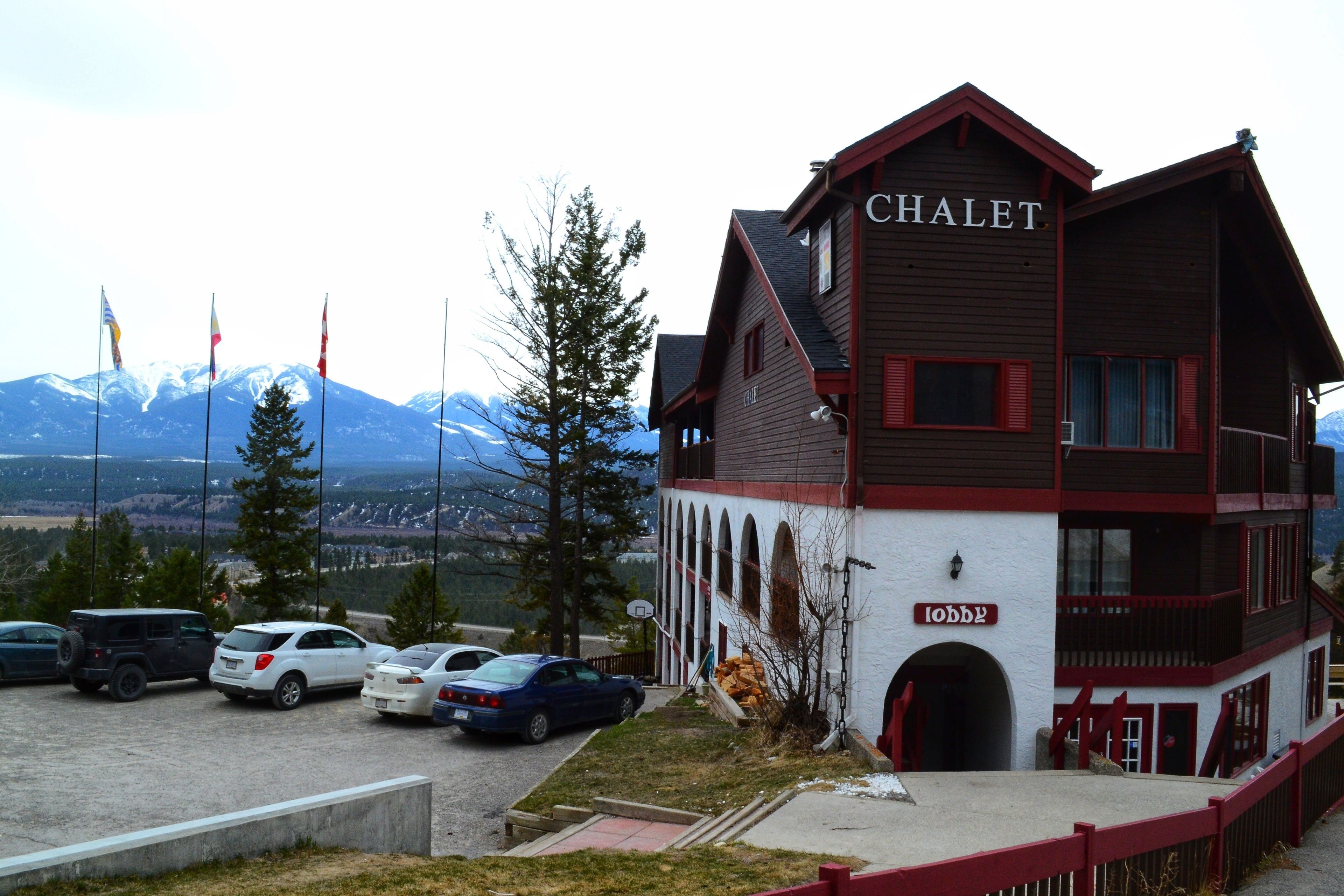 A chalet with a sign reading "CHALET" and "LOBBY" at the entrance, surrounded by parked cars and a mountainous backdrop.