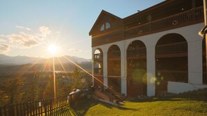 A two-story building with a balcony and arched windows, set against a mountainous backdrop.
