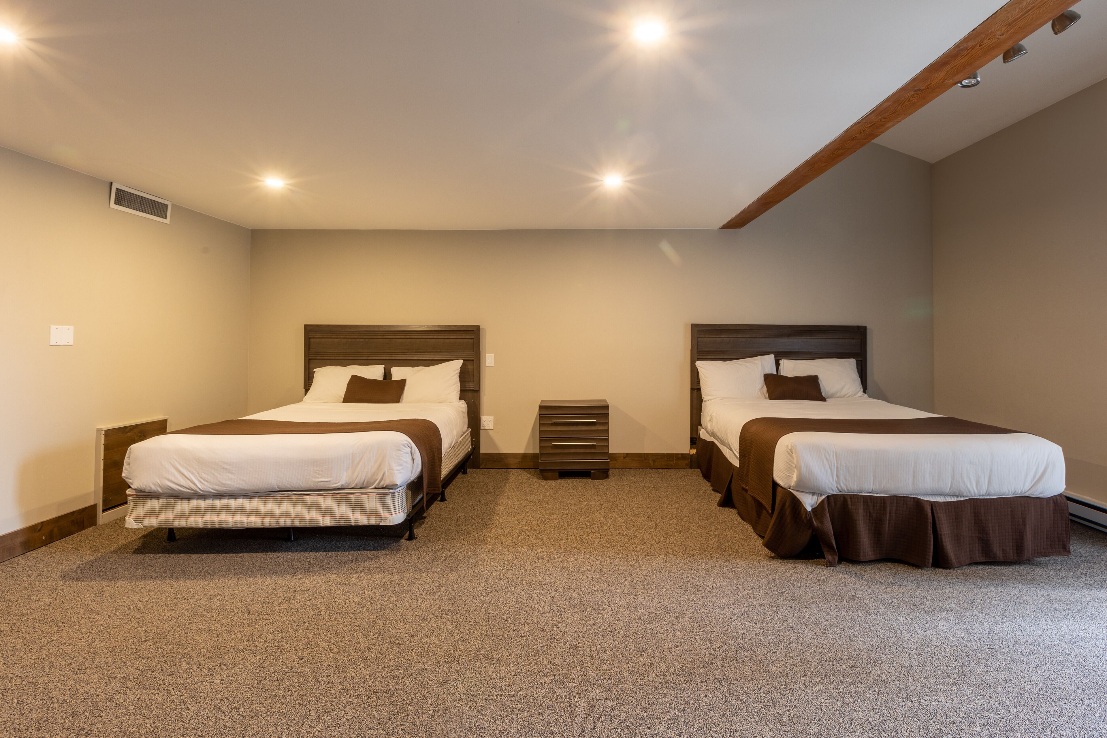 Habitación con dos camas, cada una con cabecero de madera, un pequeño calentador entre ellas y suelo alfombrado.