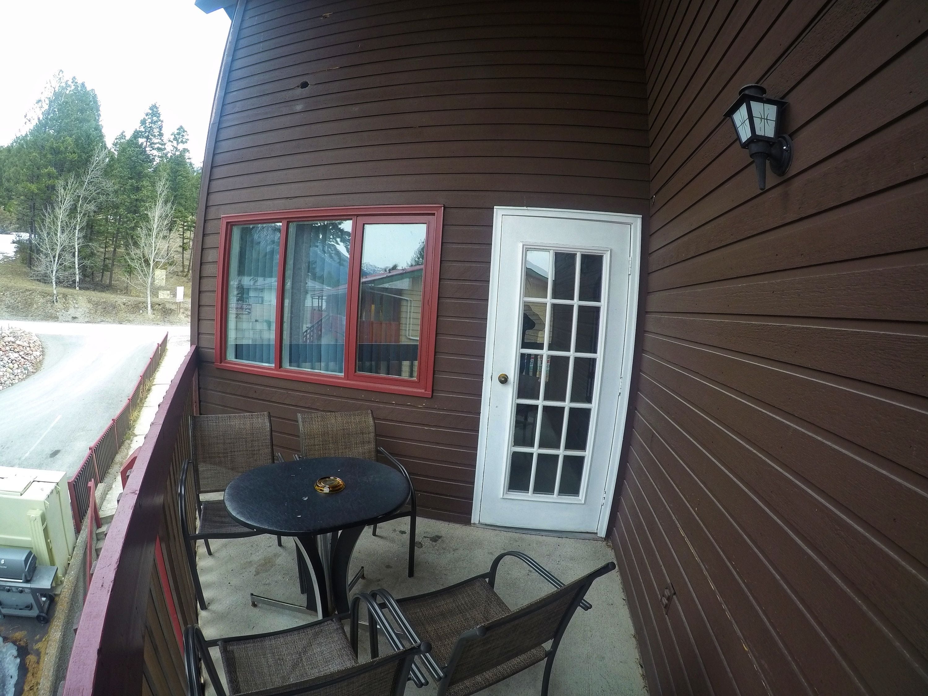 A wooden exterior with a red-framed window, a white door, and a small patio with a table and chairs.