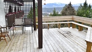 A wooden deck with a bench and chairs, overlooking a mountainous landscape.