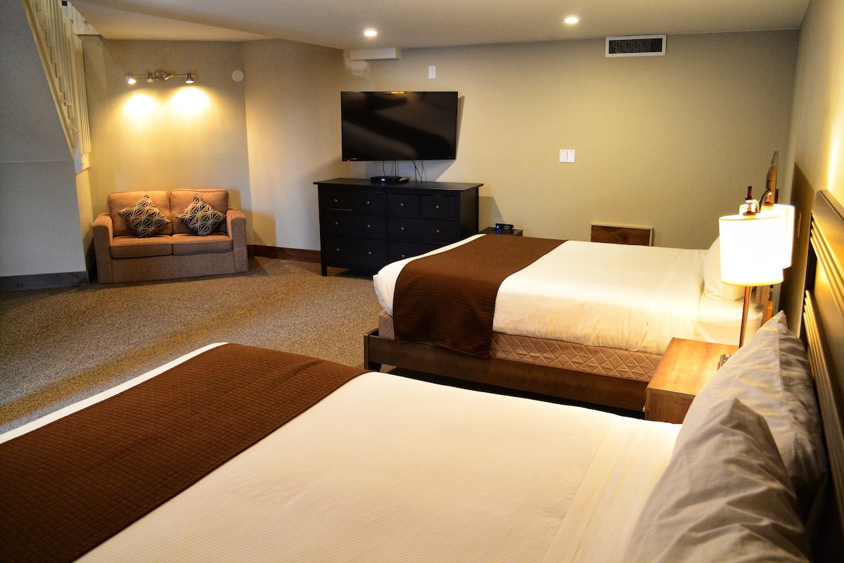 Habitación de hotel con dos camas, un sofá, un televisor y un aparador.