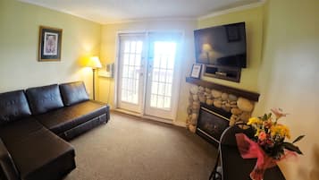 A living room with a sofa, a fireplace, a TV mounted above it, and a door leading outside.