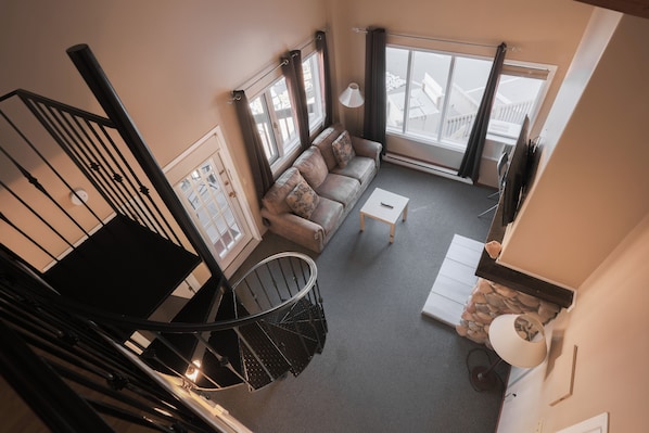 A spacious living room with a sofa, a coffee table, and a staircase with a black railing. - Radium Chalet (Radium Hot Springs)