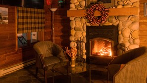 A cozy room with a stone fireplace, two armchairs, a coffee table, and a plaid curtain. - Radium Chalet (Radium Hot Springs)