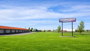 A motel with a sign reading "Northern Lights Inn & Suites" in a grassy area with a clear sky. - Northern Lights Inn & Suites (Valleyview)