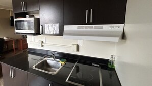 A modern kitchen with black cabinets, a microwave, a sink, and a stove. - Northern Lights Inn & Suites (Valleyview)