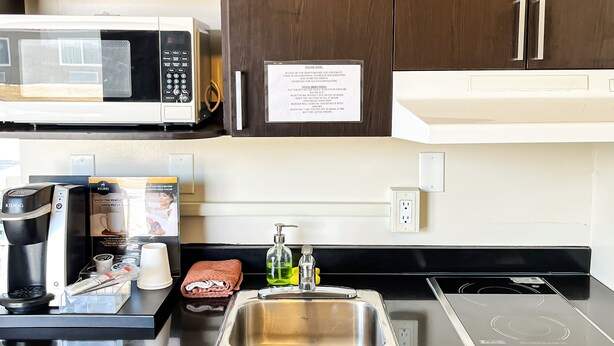 A modern kitchen with dark wooden cabinets, a stainless steel sink, a microwave, a coffee maker, and a kettle. - Northern Lights Inn & Suites (Valleyview)