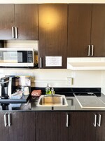 A modern kitchen with dark wooden cabinets, a stainless steel sink, a microwave, a coffee maker, and a kettle.