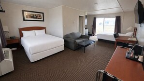 A hotel room with a large bed, a sofa, a desk, and a TV. - Northern Lights Inn & Suites (Valleyview)