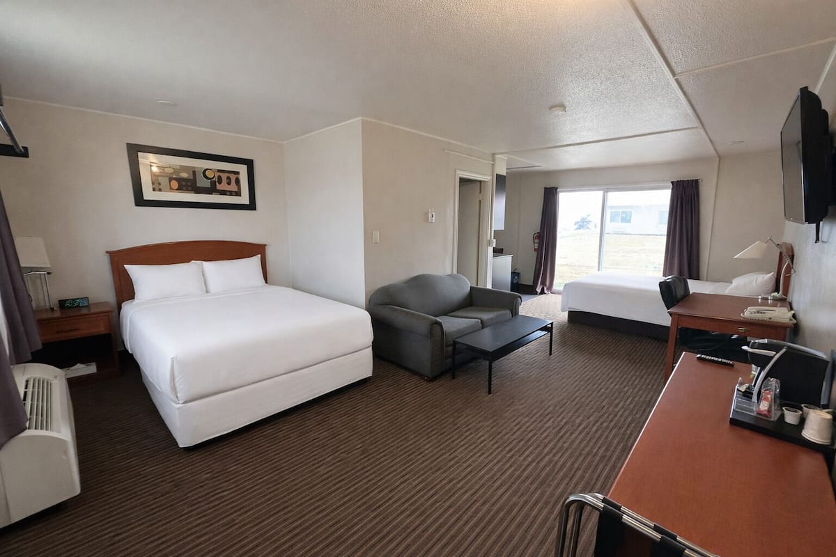 A hotel room with a large bed, a sofa, a desk, and a TV.