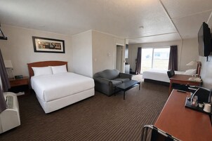 A hotel room with a large bed, a sofa, a desk, and a TV.