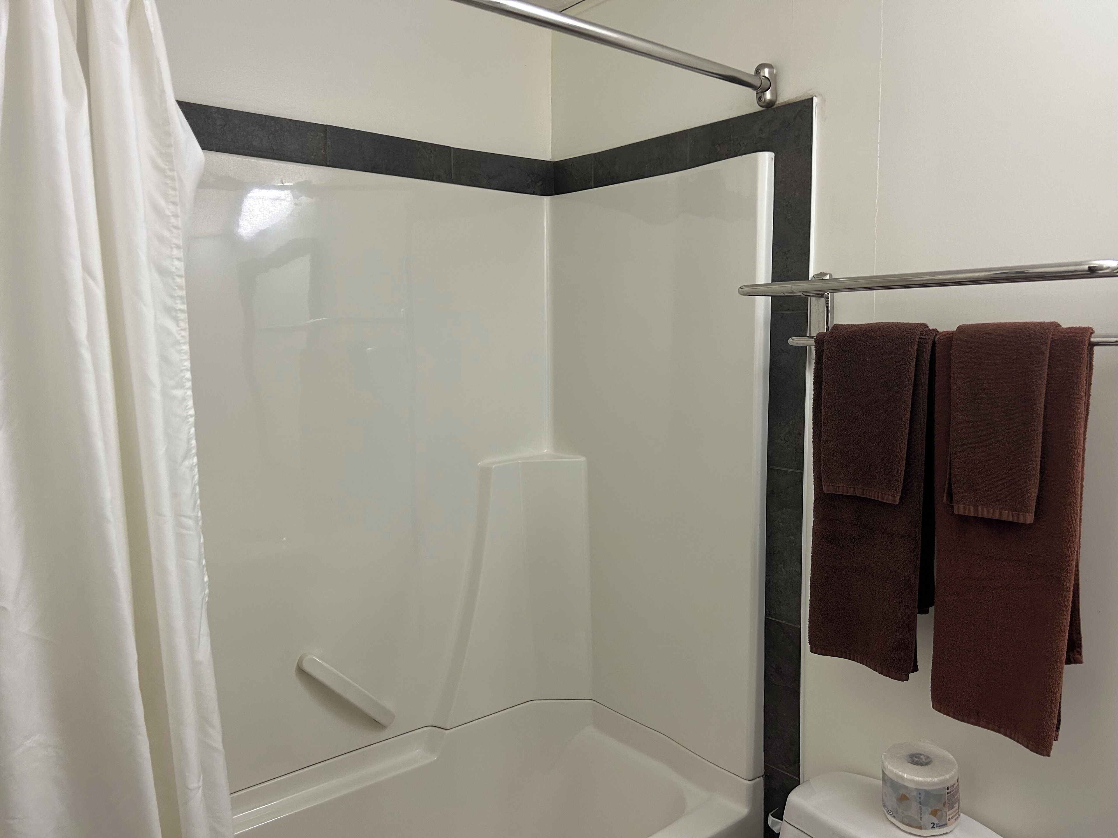 A shower area with a glass door, a towel rack with towels, and a toilet with a toilet paper roll.
