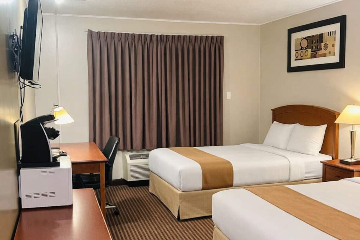 A hotel room with two beds, a desk, a chair, a television, and a framed picture on the wall.
