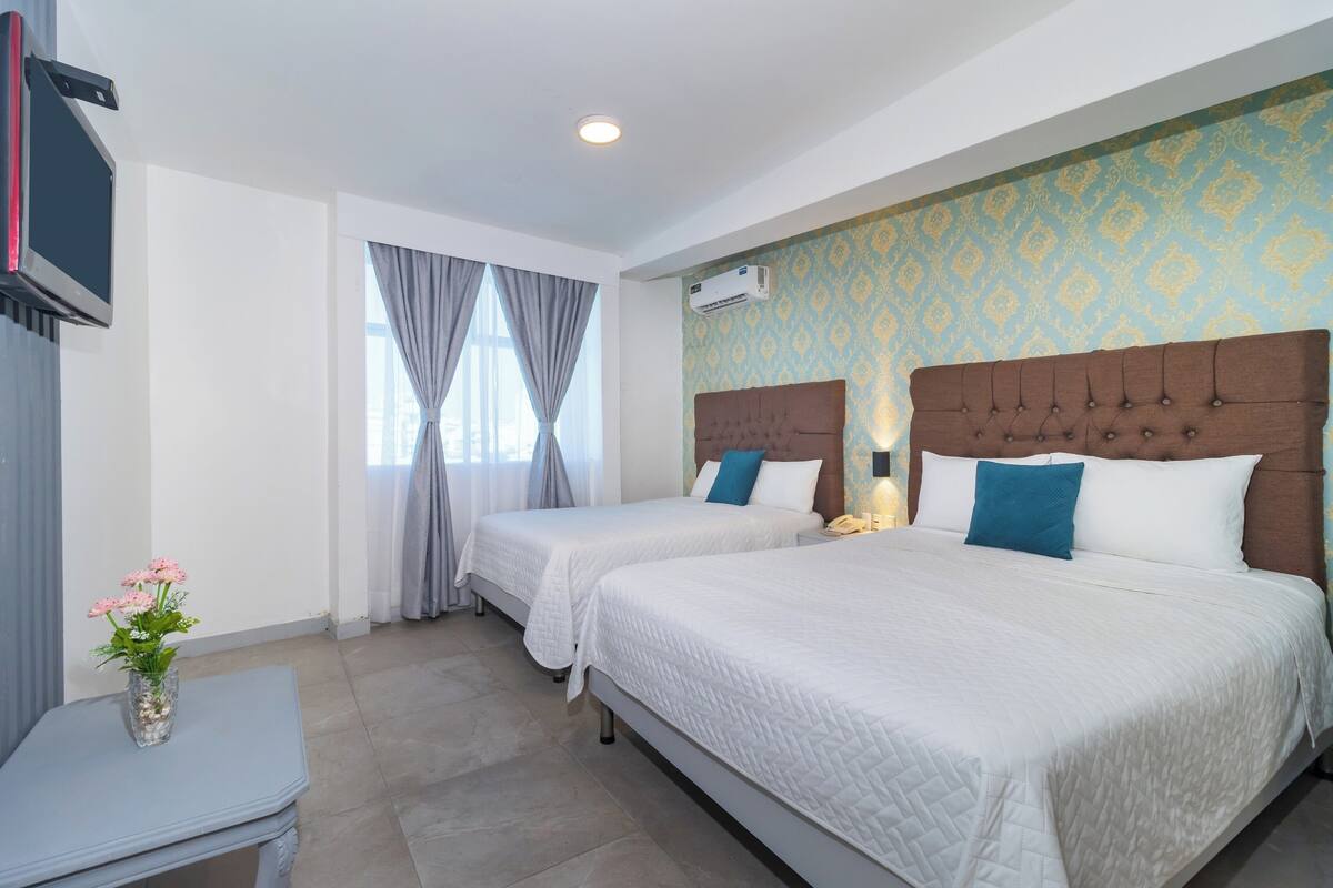 A hotel room with two beds, a TV, a vase with flowers, and a patterned wall.