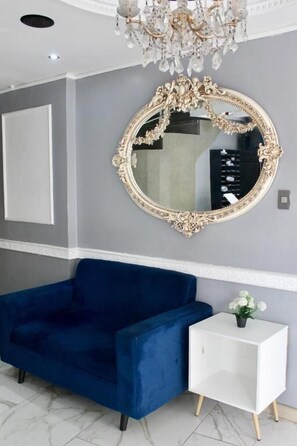 A room with a blue sofa, a white side table, and a large ornate mirror on the wall. - Hotel Presidente Internacional (Guayaquil)