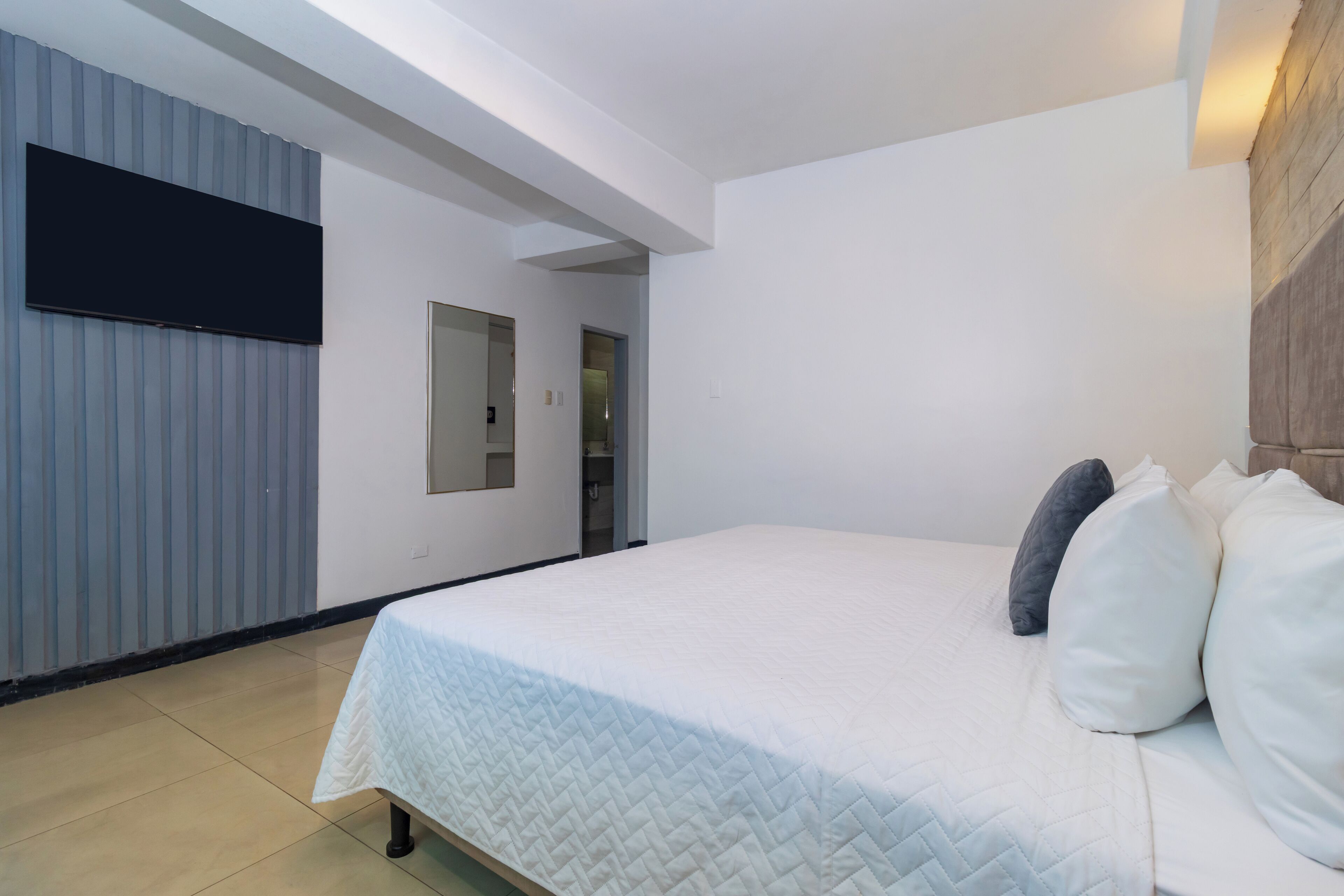 Un dormitorio con una cama grande, un televisor de pantalla plana montado en la pared y un cabecero de madera.