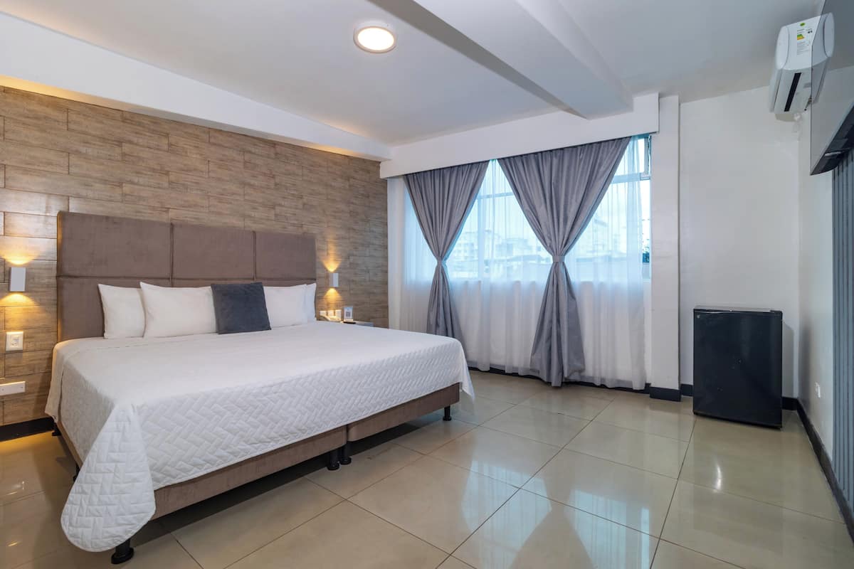 A modern hotel room with a large bed, wooden headboard, and a city view through the window.