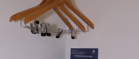 Una caja fuerte negra con cierre giratorio, perchas de madera en un colgador metálico y un cartel con instrucciones de uso.