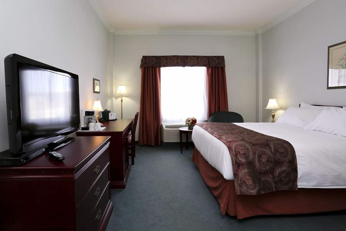A hotel room with a bed, a desk with a television, a chair, and a lamp.