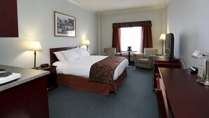 Habitación de hotel con una cama, dos lámparas de noche, un escritorio con una computadora, una silla, una mesita y un televisor.