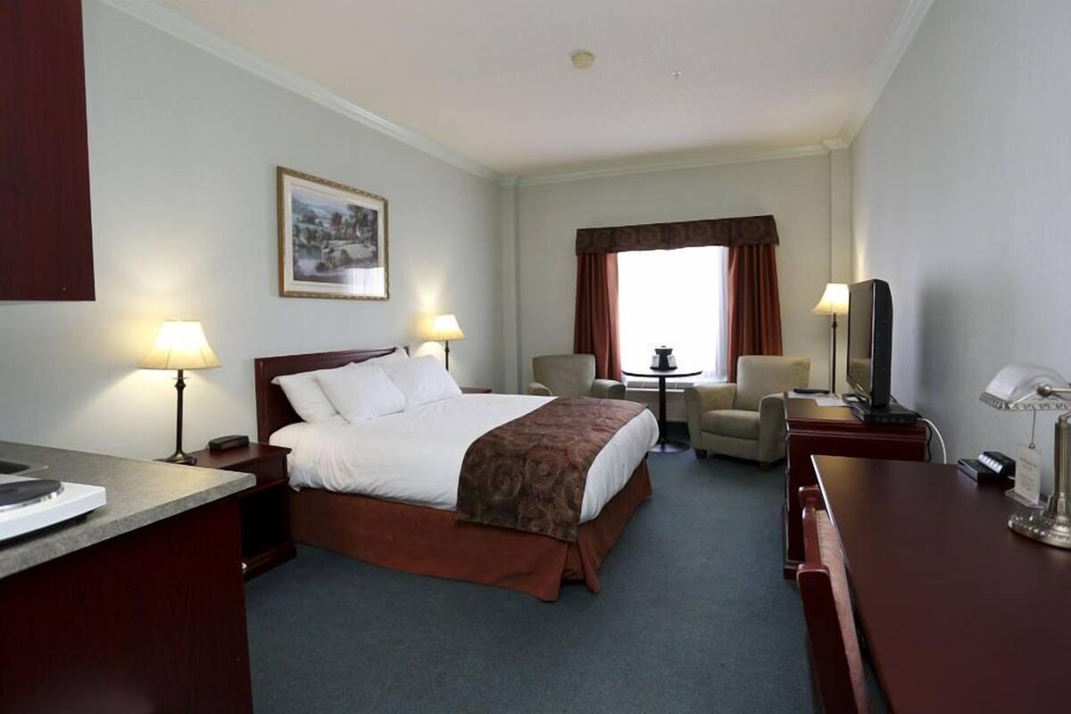 A hotel room with a bed, two bedside lamps, a desk with a computer, a chair, a small table, and a television.