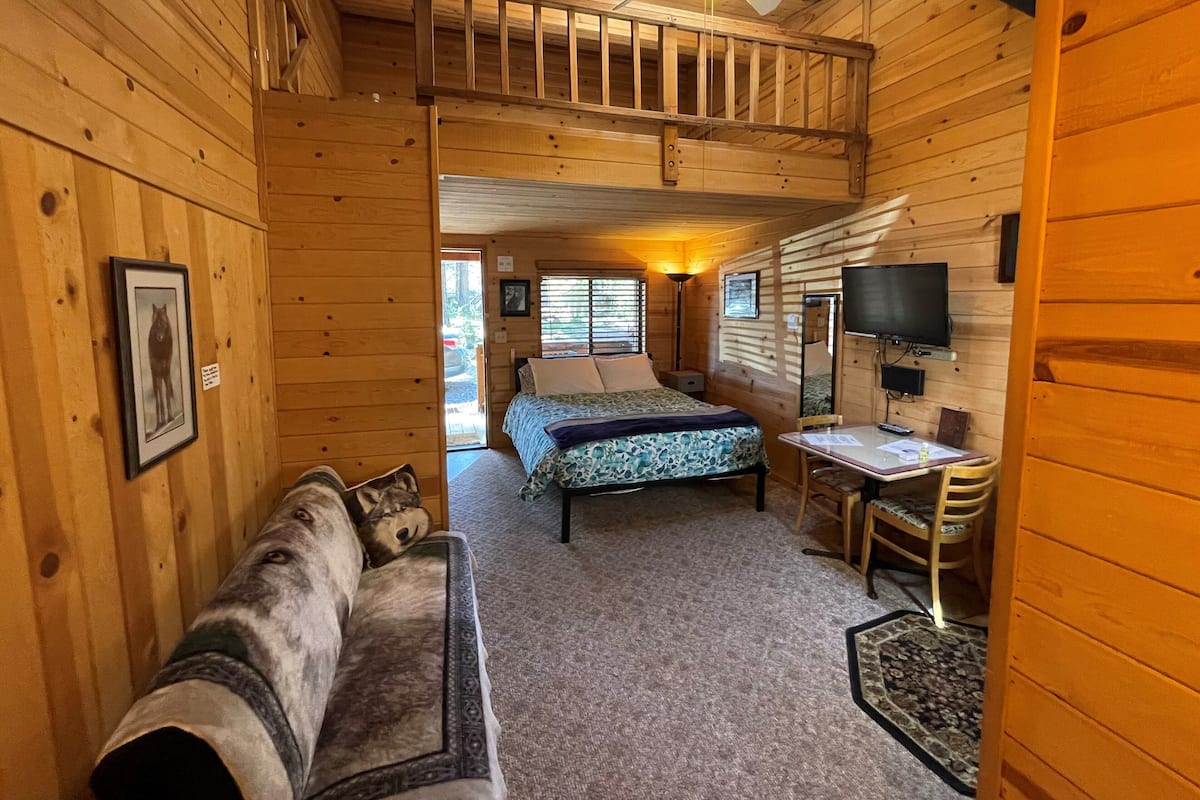 A cabin interior with a bed, a desk, a chair, a couch, and a ceiling fan.