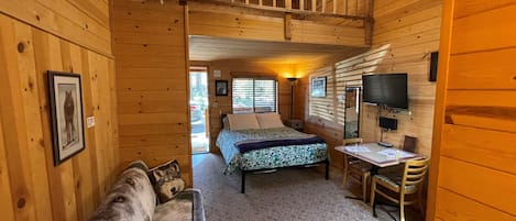 Interior de una cabaña con una cama, un escritorio, una silla, un sofá y un ventilador de techo.