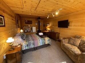 Een gezellig kamer in chaletstijl met een bed, een bank, een bureau en een televisie.
