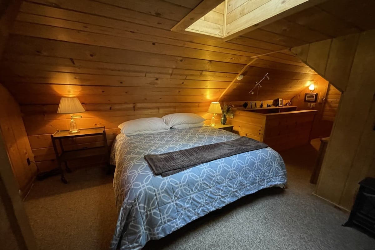 A cozy attic bedroom with a bed, two bedside lamps, a nightstand, and a wooden dresser.