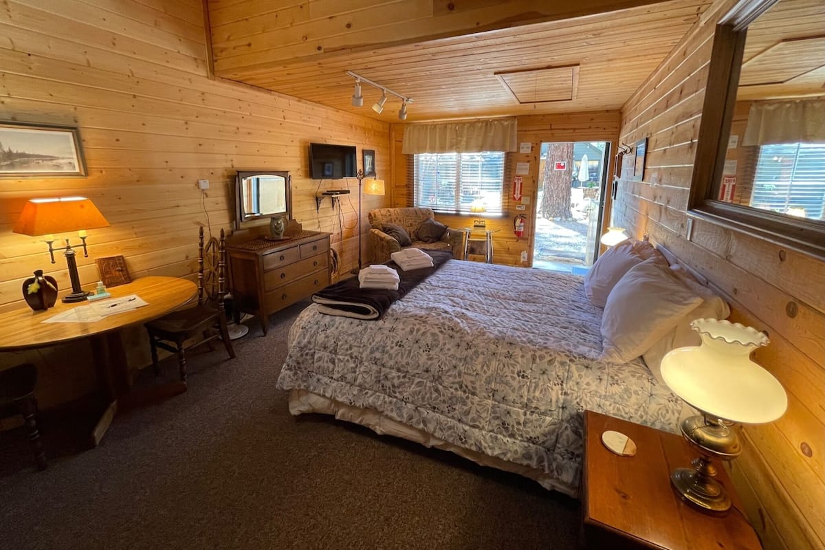 A cozy cabin-style room with a bed, a desk, a chair, a television, and a window.