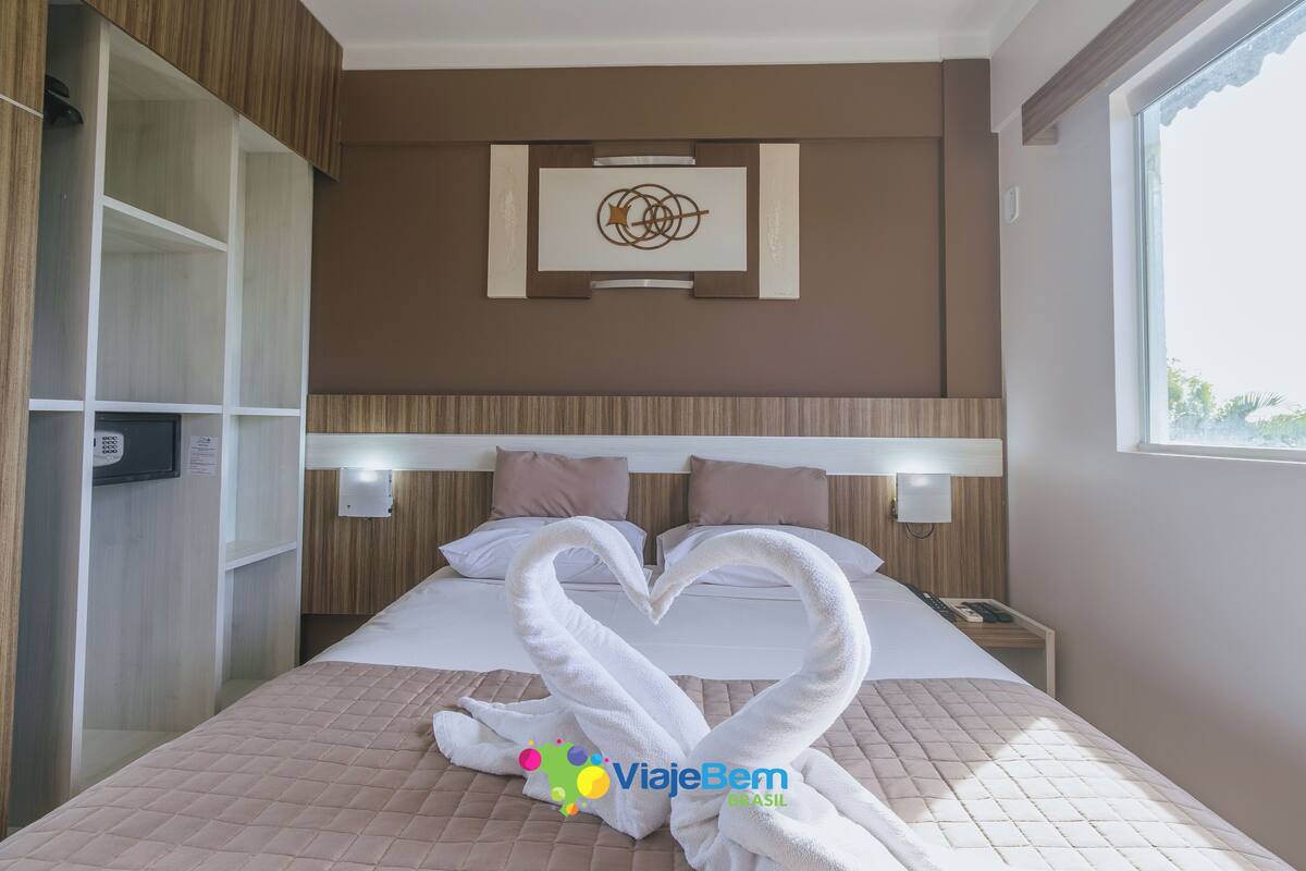 Une chambre d’hôtel avec un lit, une tête de lit, une œuvre d’art accrochée au mur et une fenêtre.