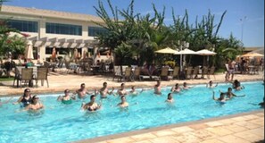 Ein Schwimmbecken mit darin badenden Personen, umgeben von Liegestühlen und Sonnenschirmen.