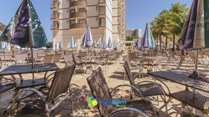 An outdoor seating area with wicker chairs and tables, umbrellas, and a tall building in the background. - diRoma Exclusive Caldas Novas (Caldas Novas)